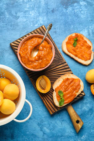 Wooden board with bowl of apricot jam and sandwiches on color backgroundの写真素材