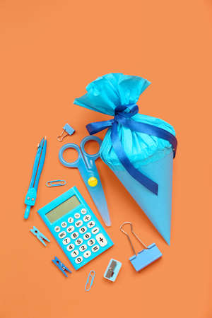 School cone with stationery supplies on orange background