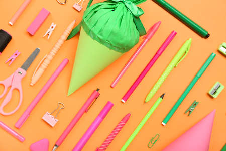 School cones with stationery supplies on orange background