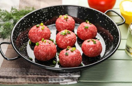 Baking dish with raw meat balls and cut green onion on color wooden background