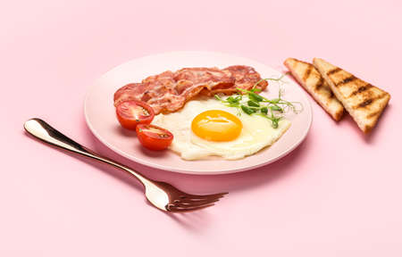 Plate with tasty fried egg, bacon and toasts on pink backgroundの写真素材