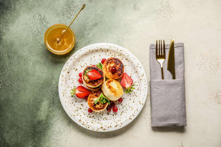 Plate with cottage cheese pancakes, cutlery and bowl with honey on grunge backgroundの写真素材