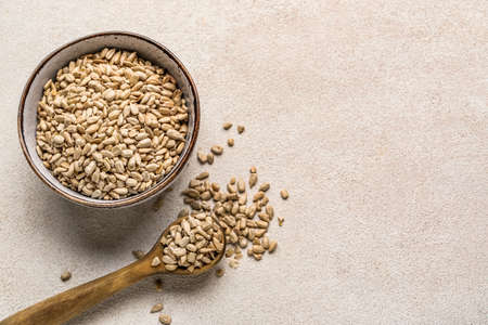 Bowl and spoon with peeled sunflower seeds on white background