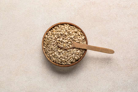 Bowl and spoon with peeled sunflower seeds on white background
