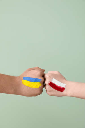 Volunteers with drawn flags of Ukraine and Poland bumping fists on green backgroundの写真素材