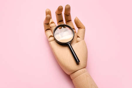 Wooden hand and magnifying glass on pink background