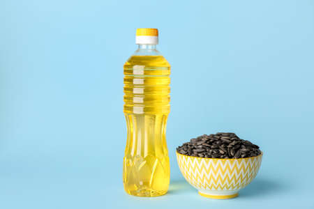 Bottle of oil and bowl with sunflower seeds on blue backgroundの写真素材