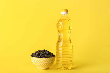Bottle of oil and bowl with sunflower seeds on yellow background