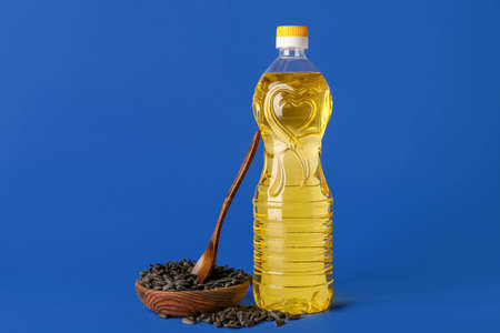Bottle of oil and wooden bowl with sunflower seeds on blue background