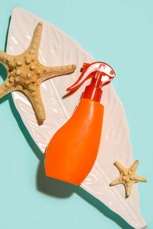 Spray bottle of sunscreen with starfishes and decorative leaf on blue backgroundの写真素材