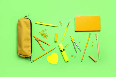 Yellow pencil case with stationery supplies and paper clips on green backgroundの写真素材