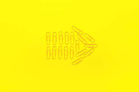 Arrow made of paper clips on yellow background