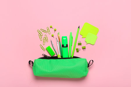 Green pencil case with paper clips and school stationery on pink backgroundの写真素材