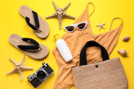 Sunscreen cream with beach accessories and photo camera on yellow background