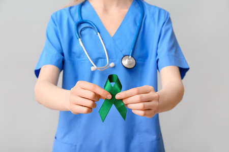 Female doctor with green ribbon and stethoscope on gray background. Liver cancer concept