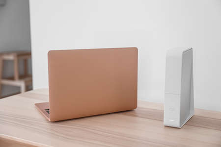 Modern laptop and wi-fi router on table near light wallの写真素材