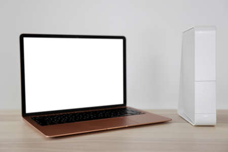 Modern laptop and wi-fi router on table near white wallの写真素材