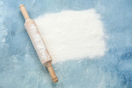 Rolling pin with wheat flour on blue background
