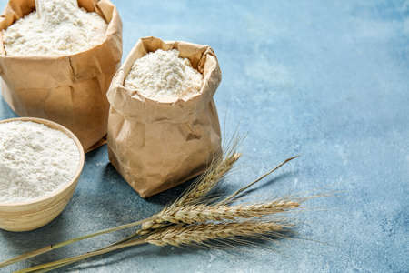 Wheat ears, paper bags and bowl with flour on blue background