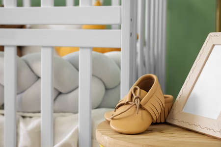 Table with baby booties and frame near crib, closeupの写真素材