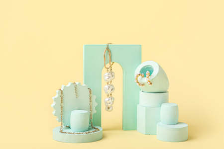 Showcase pedestals with stylish jewelry on color background
