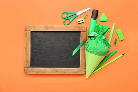 Chalkboard with school cone and stationery supplies on orange background