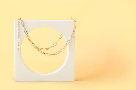 Showcase pedestal with elegant necklace on color background