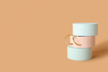 Showcase pedestal with golden earrings on beige background