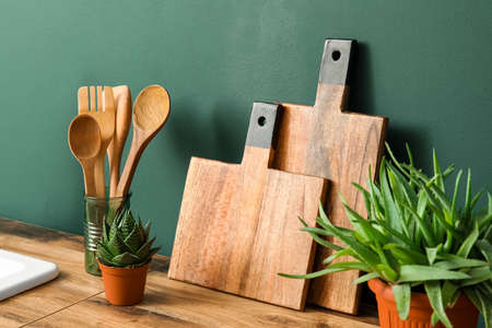 Wooden cutting boards, spatulas and houseplants on counter near green wallの写真素材