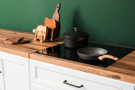 Counters with cutting boards, cooking pot, frying pan and stove near green wall