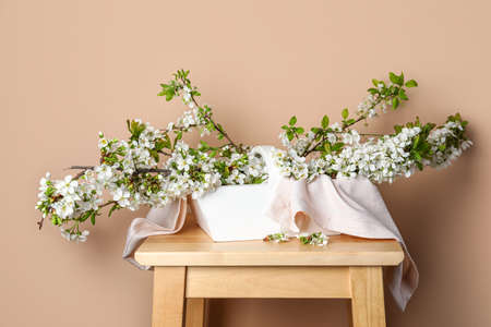 Basket with beautiful blooming tree branches on table near color wall
