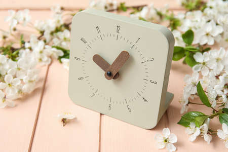 Blooming spring branches and clock on color wooden background