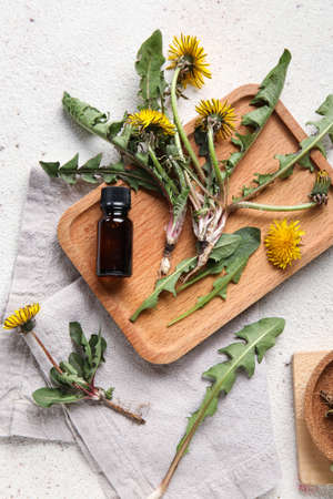 Yellow dandelions with cosmetic bottle, wooden board and napkin on white backgroundの写真素材