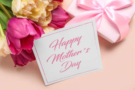Card with text HAPPY MOTHER'S DAY, bouquet of tulips and gift box on pink background, closeup
