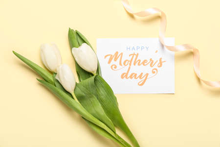 Card with text HAPPY MOTHER'S DAY, white tulips and ribbon on beige backgroundの写真素材