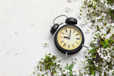 Blooming spring branches and alarm clock on white background, top view