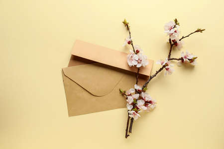 Beautiful blooming spring branch and envelopes on light color background, top viewの写真素材