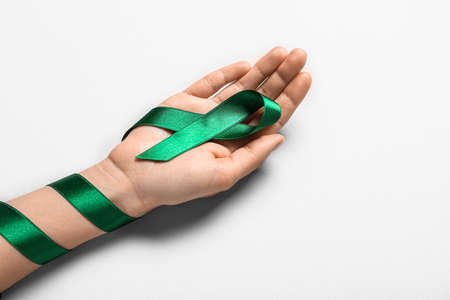 Hand with green ribbon on light background. Liver cancer concept