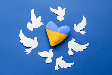 Heart in colors of Ukrainian flag and paper doves as symbol of peace on blue backgroundの写真素材