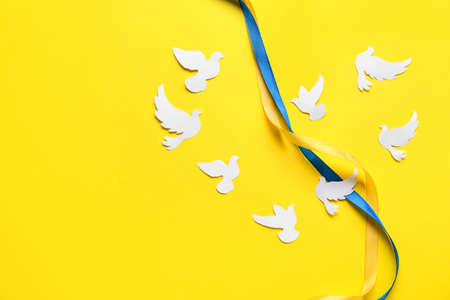 Ribbon in colors of Ukrainian flag and heart made of paper doves as symbol of peace on yellow backgroundの写真素材