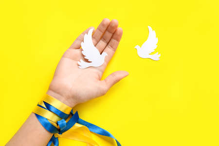 Hand with paper doves and ribbons in colors of Ukrainian flag on yellow backgroundの写真素材