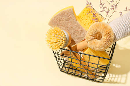 Basket with set of cleaning supplies, towel and flowers on color background, closeup