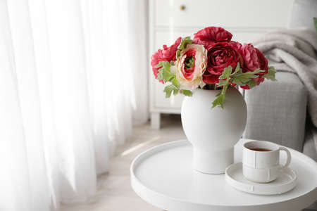 Vase with bouquet of beautiful flowers and cup of coffee on table in room
