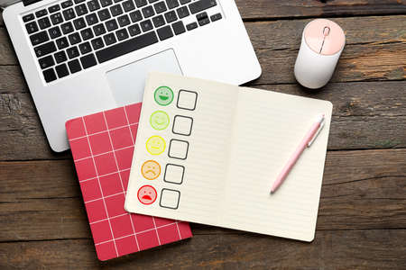 Notebooks with satisfaction rating, pen and laptop on wooden background