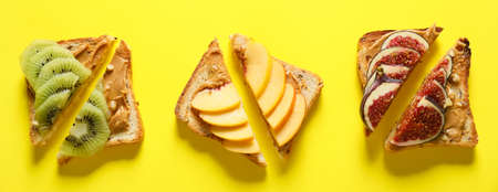 Tasty sweet sandwiches with peanut butter ad fresh fruits on yellow background