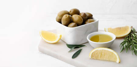 Green olives, oil and lemon slices on white table