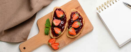 Wooden board with tasty toasted bread and sweet strawberry jam on white table