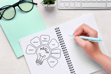 Woman writing in notebook at table. Agile concept