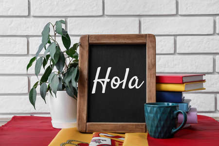 Chalkboard with text HOLA (HELLO), cup and books on tableの写真素材