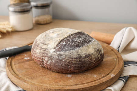 Cutting board with fresh bread on kitchen counter near gray wall, closeup